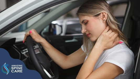 Female with one hand on her neck in pain and the other hand on the steering wheel